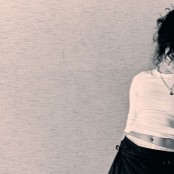 A woman with dark curly hair leaning against a wall